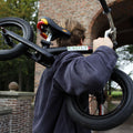 Een medeoprichter houdt een zwarte kinderfiets vast en kijkt naar de natuur en een bakstenen gebouw. - BikeFlip