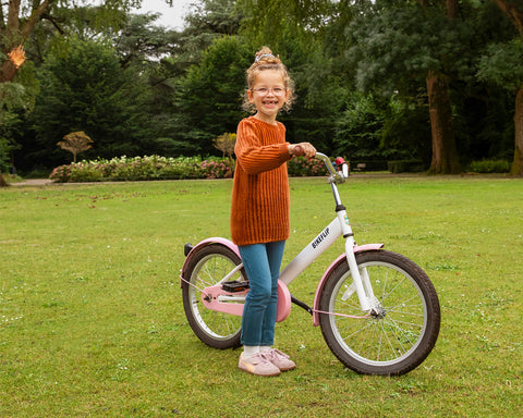 Blij meisje rijdt op een wit-roze fiets in het park - BikeFlip