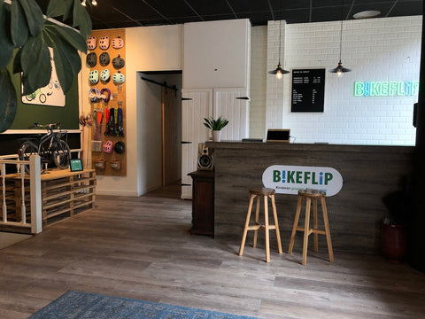 Een overzicht van een conceptstore, klantenservice bij de balie, winkelborden, accessoires zoals helmen, sloten, manden en een fiets op display. - BikeFlip