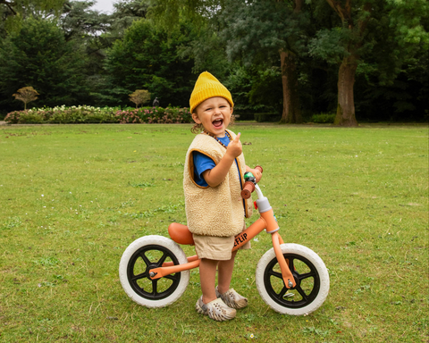 Blije jongen rijdt op een oranje fiets in het park - BikeFlip