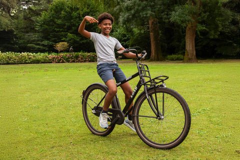 Blije jongen rijdt op een zwarte fiets in het park. - BikeFlip