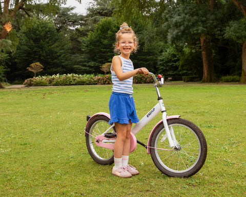 Blij meisje rijdt op een wit-roze fiets in het park - BikeFlip