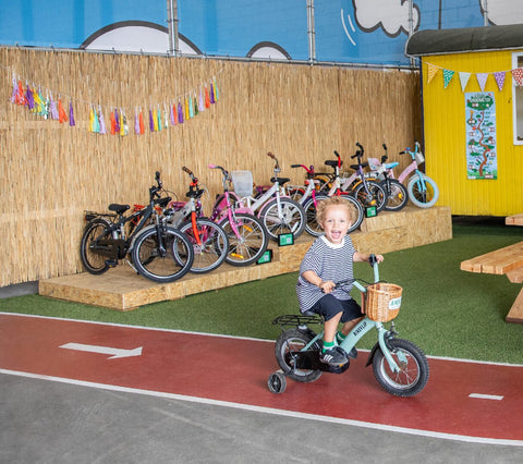 Blije jongen rijdt op een fiets voor een verscheidenheid aan fietsen en racet op een fietsbaan. - BikeFlip